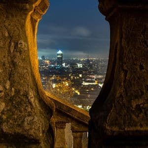 Skyline cittadino illuminato di notte, visto attraverso un arco in pietra dalla luce calda.