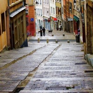 Una ripida e bagnata strada acciottolata scende attraverso uno stretto vicolo fiancheggiato da alti e colorati edifici storici.