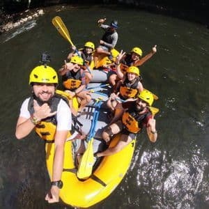 Un groupe WeRoad prend un selfie en hauteur en faisant du rafting sur une rivière, dans un bateau jaune, tous souriants et portant des casques.