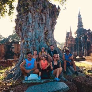 Un grupo de WeRoad posa para una foto al pie de un gran árbol antiguo, con ruinas de templos de fondo, durante el atardecer.