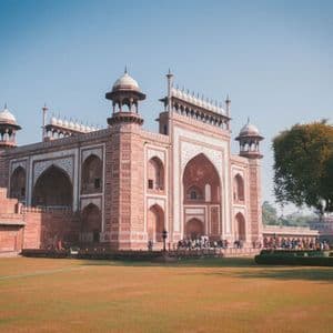 Una puerta ornamentada de arenisca roja con detalles de mármol blanco se alza detrás de un gran césped verde, con gente reunida cerca de la entrada.