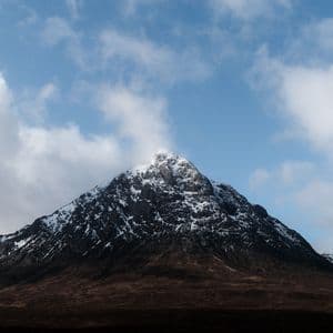 Una montaña rocosa cubierta de nieve se alza bajo un cielo azul con nubes blancas dispersas.