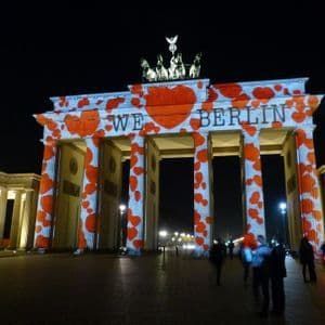 La Porta di Brandeburgo è illuminata di notte con una proiezione di cuori rossi e il testo "WE ❤️ BERLIN" sulla sua facciata.