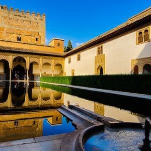 Un cortile in stile moresco con una lunga vasca riflettente che rispecchia gli edifici circostanti sotto un cielo azzurro limpido.