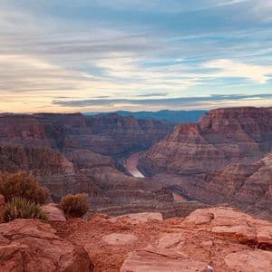 Ein weiter Blick auf einen tiefen Canyon mit einem sich schlängelnden Fluss, von einem felsigen Aussichtspunkt unter einem bewölkten Himmel bei Sonnenuntergang.