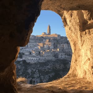 Un antico borgo in pietra adagiato su un fianco di collina, con un campanile, visto attraverso l'apertura di una grotta durante l'ora d'oro.