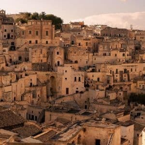Un fitto paesaggio urbano di antichi edifici in pietra color sabbia, costruiti fittamente su una collina sotto un cielo velato.