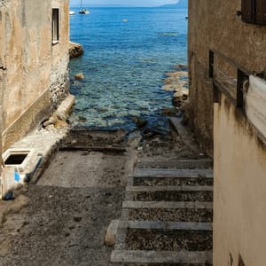 Una scalinata in pietra scende attraverso un vicolo stretto tra due edifici, conducendo al mare azzurro e limpido.