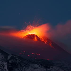 Un vulcano erutta di notte, vomitando lava incandescente e scintille dal suo cratere nel cielo scuro, mentre è circondato dal fumo.