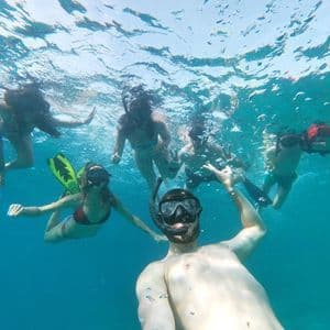 A WeRoad group trip takes an underwater selfie while snorkeling together in clear blue water.