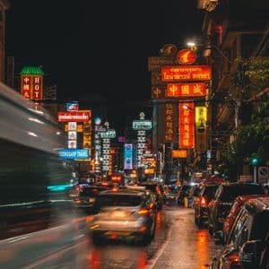 Una strada cittadina trafficata di notte, piena di traffico di auto e illuminata da insegne al neon colorate che si riflettono sull'asfalto bagnato.