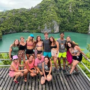 Un gruppo WeRoad in posa per una foto su un punto panoramico in legno, con vista su una laguna turchese circondata da scogliere verdi e lussureggianti.