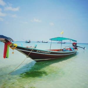 Ein traditionelles Longtail-Boot, mit Bändern geschmückt, gleitet in ruhigem, türkisfarbenem Wasser, mit einer grünen Insel am Horizont.