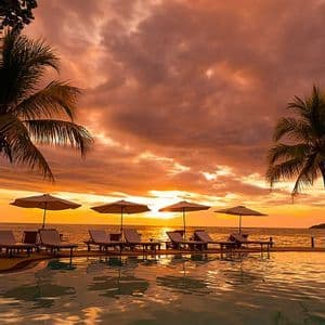 Sdraio e ombrelloni su una terrazza a bordo piscina, con vista sull'oceano durante un tramonto arancione.