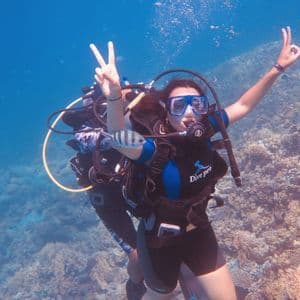 Una donna in un viaggio di gruppo WeRoad si immerge sopra una barriera corallina, mostrando i segni di pace e OK alla telecamera.