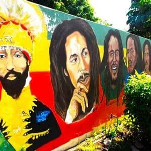 Ein farbenfrohes Wandgemälde im Freien zeigt ein großes Porträt von Haile Selassie I. neben mehreren Porträts des Musikers Bob Marley.