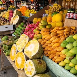 Ein Obstmarktstand ist vollgepackt mit einer Vielzahl tropischer Früchte, darunter geschnittene Jackfrucht, Mangos, Drachenfrucht und Durian.