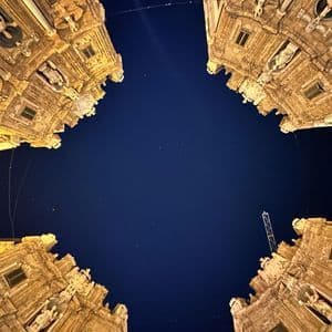 Una prospettiva dal basso di quattro angoli di palazzi sfarzosi illuminati che incorniciano un cielo notturno buio e stellato.