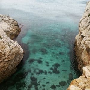 Una stretta caletta con acque limpide e turchesi, incorniciata da due grandi scogliere rocciose, vista dall'alto.