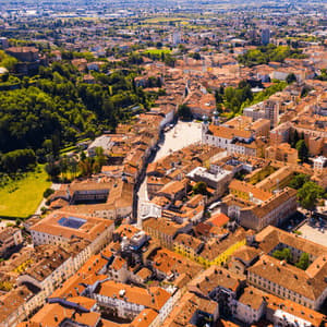 Veduta aerea di una città europea con tetti in terracotta, una piazza centrale e alberi verdi circostanti.