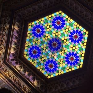 Una vidriera hexagonal en el techo, con un diseño floral geométrico y colorido en tonos azules, verdes y amarillos.