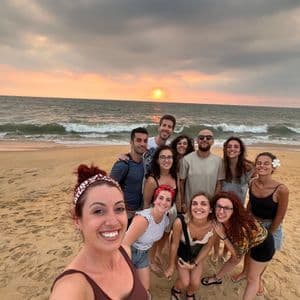Un viaggio di gruppo WeRoad si fa un selfie su una spiaggia sabbiosa mentre il sole tramonta sull'oceano.