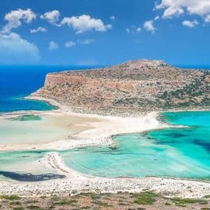 Vista aerea di un'isola rocciosa con una lingua di sabbia che separa una laguna turchese dal mare blu intenso.