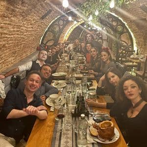 Un gruppo WeRoad in costume di Halloween è seduto a un lungo tavolo da pranzo in una cantina con archi in mattoni, sorridendo alla fotocamera.