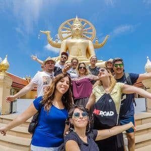 Eine WeRoad-Gruppe posiert für ein Foto auf den Stufen vor einer großen, goldenen Buddha-Statue unter klarem blauem Himmel.