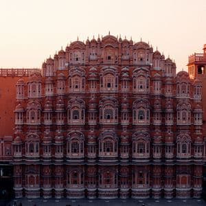 Una elaborada fachada de palacio de arenisca rosa con cientos de pequeñas ventanas de celosía bajo un cálido cielo de atardecer.