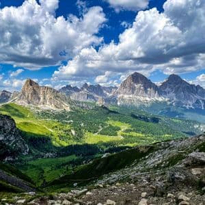 Una vista panoramica di una catena montuosa rocciosa con valli verdi e foreste sotto un cielo blu con nuvole bianche e gonfie.
