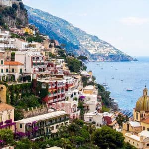 Una vista panoramica di una colorata città costiera costruita su una scogliera, che si affaccia su un mare blu con tante barche.