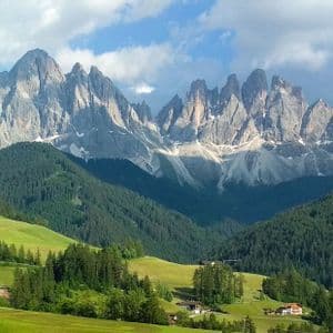 Un petit village avec son église, niché dans une vallée verdoyante au pied de collines boisées et d'une chaîne de montagnes rocheuses et déchiquetées.