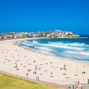 Une vue plongeante d'une plage de sable bondée par une journée ensoleillée, avec des gens qui se baignent dans l'océan et bronzent sur le rivage.