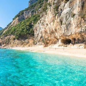 Aguas turquesas se encuentran con una playa de arena aislada a los pies de un gran acantilado escarpado bajo un cielo despejado.