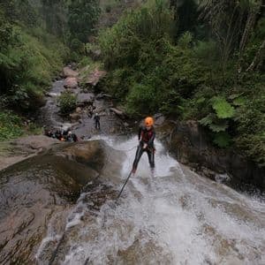 A person from a WeRoad group trip rappels down a fast-flowing waterfall, wearing a helmet and wetsuit.