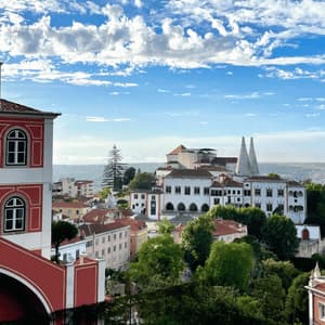 A red and white building overlooks a historic town with a palace featuring two white conical chimneys, under a partly cloudy sky.