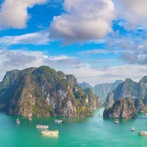 Veduta dall'alto di imbarcazioni che navigano su acque turchesi tra isole calcaree ricoperte di giungla, sotto un cielo azzurro brillante.