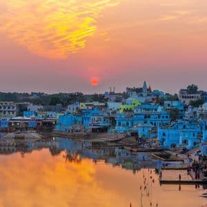Una città di edifici blu costruita lungo la riva di un lago si riflette nell'acqua calma durante un tramonto vibrante.