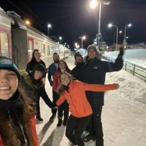 Un grupo de WeRoad se toma una selfie en una plataforma de tren nevada por la noche, de pie junto a un tren detenido.
