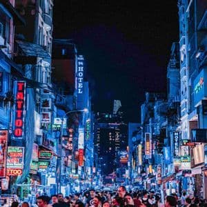 Eine belebte Stadtstraße bei Nacht, auf der Menschen unter hohen Gebäuden mit leuchtenden blauen und roten Neonschildern entlanglaufen.