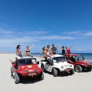 Un viaje en grupo de WeRoad posando en tres vehículos todoterreno en una playa de arena con el océano y un cielo azul de fondo.