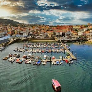 Una vista panorámica aérea de un colorido pueblo costero con un puerto lleno de barcos amarrados bajo un cielo nublado dramático.