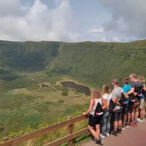 Un grupo de WeRoad se asoma tras una valla de madera, contemplando un vasto cráter volcánico verde con un lago en el fondo.