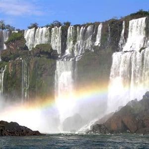 Una gran cascada cae por un acantilado rocoso y verde, formando un arcoíris en la niebla a sus pies.