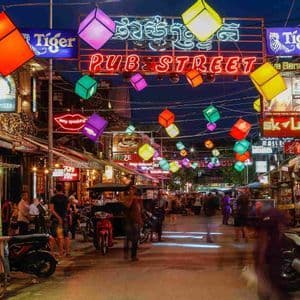 Una calle concurrida por la noche iluminada por un letrero de neón 'Pub Street' y linternas cúbicas de colores colgando.