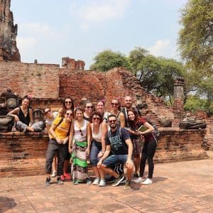 Un groupe WeRoad en voyage sourit et pose pour une photo au milieu de ruines de temples anciens en briques rouges, sous un ciel dégagé.