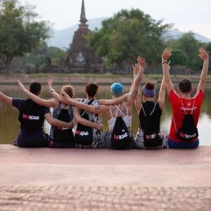 Un grupo de WeRoad en un muelle con los brazos levantados, frente a un templo histórico al otro lado del agua.
