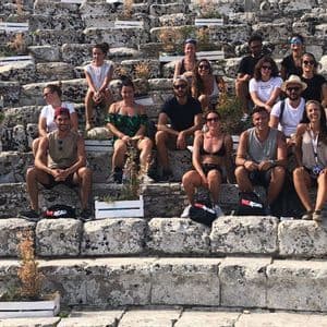 Un gruppo WeRoad in viaggio posa per una foto seduto sui grandi gradini di pietra di un antico anfiteatro.