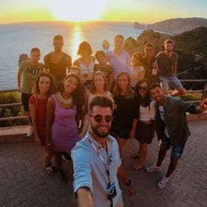 Un gruppo WeRoad in viaggio che posa per un selfie su un punto panoramico con vista mare al tramonto.